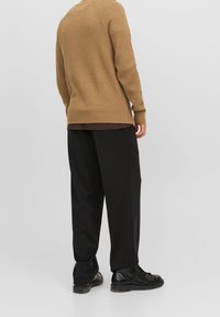 Brun, ribbad tröja med rund hals, i kombination med lösa svarta byxor och svarta stövlar. Materialen har en strukturerad yta.