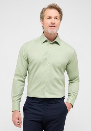 Hellgrünes Langarmhemd mit Knopfdesign, mit Kragen und einem subtilen strukturierten Stoff, kombiniert mit dunkelblauen Hosen.