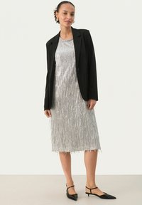 Silberfransen-Kleid mit einem schwarzen Blazer, eleganter Silhouette, knielang, detaillierte Textur und kombiniert mit spitzen schwarzen Schuhen.