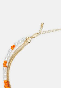 Colar em tom de ouro com pérolas brancas, realces laranja e uma corrente de metal texturizada. Inclui um fecho tipo lagosta e elos ajustáveis.
