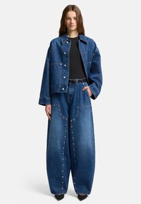 Denim jacket with a relaxed fit, button closure, and pocket detail, paired with wide-leg denim trousers featuring a high waist and contrast stitching.