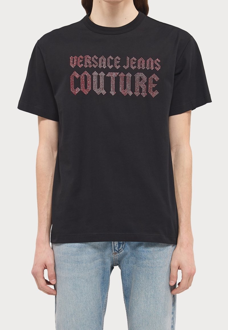Černé bavlněné tričko s výrazným nápisem "Versace Jeans Couture" v červené a stříbrné barvě v moderním písmu na hrudi. Krátké rukávy.