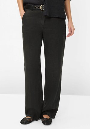 Pantalon noir fuselé avec poches avant, accompagné d’une ceinture noire avec une boucle double anneau dorée et des chaussures noires tissées à enfiler.