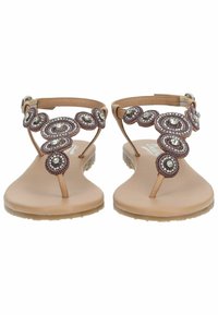 Sandali piatti in morbido ocra con design a spirale. Presentano dettagli metallici e una cinghia alla caviglia regolabile. Sottopiede testurizzato per il comfort.