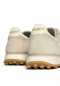 Baskets en suède beige avec un empiècement en cuir blanc au niveau du talon, semelle en caoutchouc rond et logo de marque embossé en or sur le talon.