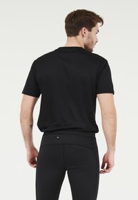 Svart atletisk t-shirt med korta ärmar, slät textur och en avslappnad passform, tillsammans med åtsittande svarta leggings med dragkedjefickor.