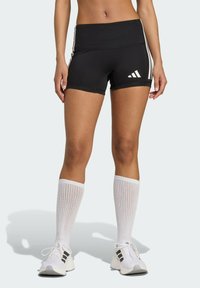 Czarne szorty sportowe z wysokim stanem, z białymi paskami bocznymi i logo Adidas. Połączone z białymi skarpetami do kolan i butami.