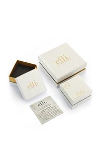 Tre hvide smykkebokse og én kasse med guldkanter og guldtryk. En struktureret kvadratisk kort ligger i nærheden med produktinformation.