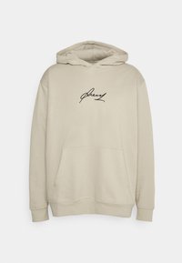 Felpa beige realizzata in morbido tessuto. Presenta una tasca a marsupio e una firma ricamata nera sul petto. Includecordini nel cappuccio.