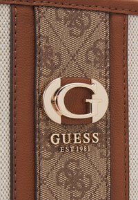 Materiale marrone testurizzato con un logo dorato e il testo "GUESS EST 1981". Presenta un motivo di G su uno sfondo marrone. Accentuato con pelle color cuoio.