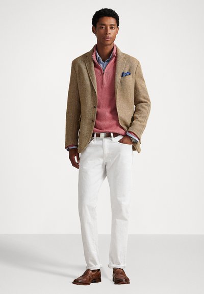 Καφέ σακάκι σε σχέδιο ριγέ με ροζ πουλόβερ, μπλε πουκάμισο με γιακά, λευκά παντελόνια και καφέ δερμάτινα παπούτσια, με μαντηλάκι τσέπης σε σχέδιο.