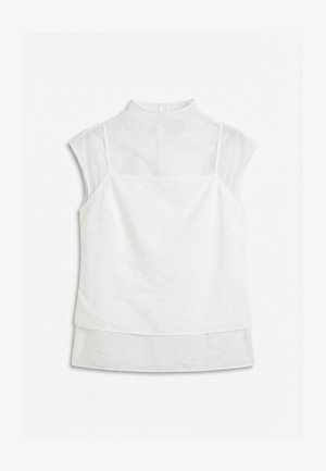 Blouse blanche sans manches à couches avec panneau supérieur translucide et col montant, étalée à plat sur un fond blanc.