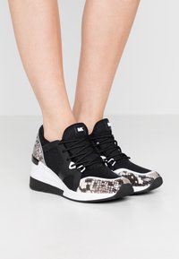 Zapatillas en blanco y negro con un patrón de piel de serpiente texturizado en los laterales, tejido de malla y cordones negros. Suela gruesa para mayor altura.