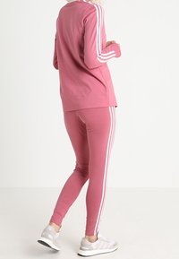 Rosa träningsset som består av en långärmad topp och åtsittande leggings med vita sidostripes. Materialet verkar mjukt och har en avslappnad passform.