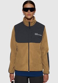 Fleece jack met een tan lichaam en een donkergrijze bovenkant, hoge kraag en ritssluiting zak. "HALO 19681972" in het wit gedrukt.
