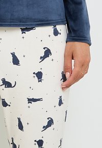 Maglia a maniche lunghe blu marino abbinata a pantaloni color crema con silhouette di gatti blu marino e motivi a stella, realizzata in tessuto morbido e confortevole.