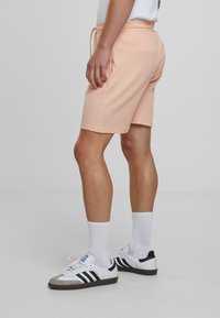 Perzikkleurige katoenen shorts met een gestructureerd oppervlak, elastische tailleband en zijvakken, gecombineerd met witte sokken en zwart-witte sneakers.