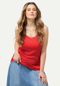 Top a maniche lunghe rosso a coste con scollatura a V, abbinato a una gonna di jeans azzurro chiaro. Il top ha una silhouette aderente e una texture liscia.