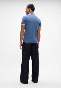 Polo bleu clair avec un col, bord blanc, associé à un jean en denim foncé et lâche. Accent sur la vue arrière et la forme des vêtements.