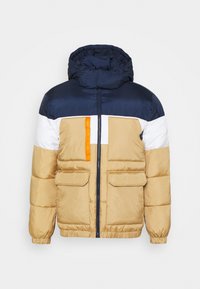 Vadderad jacka i beige, marinblå och vit. Har en huva, två framfickor och en orange accentetikett. Strukturerad tyg med ett quiltat mönster.