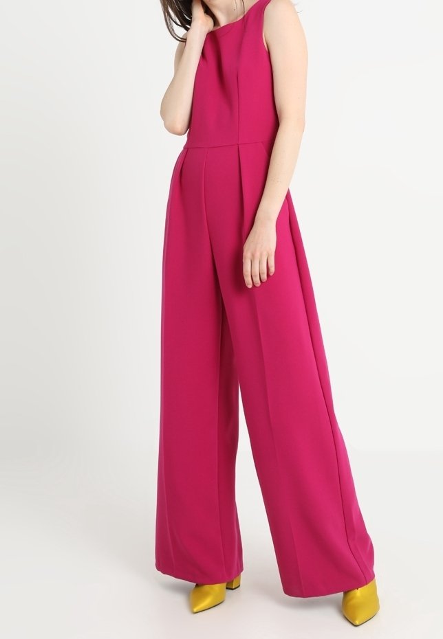 Combinaison sans manches fuchsia avec des jambes larges, dotée de plis à la taille et complétée par des chaussures à talons jaunes. Texture de tissu lisse.
