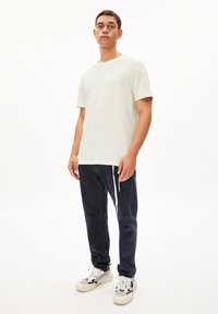 T-shirt coupe classique gris clair en coton, associé à un jean bleu foncé avec détail de cordon de serrage. Complété par des chaussures de sport blanches et noires.