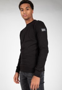 Felpa nera a maniche lunghe realizzata in morbidi misti cotone, con collo a girocollo a coste e un patch con il logo "WRONG FRIENDS" sulla manica.