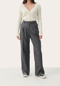 Lichtbeige geribde cardigan met een diepe V-halslijn en knopen, gecombineerd met hoog-wijde, losse grijze ruitbroeken en zwarte sneakers.