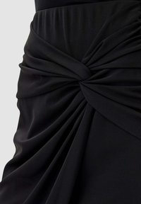 Abito nero con tessuto arricciato e un dettaglio a nodo intrecciato in vita, che crea morbide pieghe e texture su tutto il materiale.