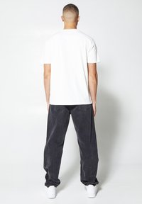 White cotton t-shirt with short sleeves, paired with loose-fitting dark grey jeans. White sneakers complete the outfit.