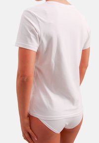 Biała bawełniana koszulka z krótkim rękawem, okrągłym dekoltem i luźnym krojem, widoczna od tyłu, zestawiona z białymi majtkami.