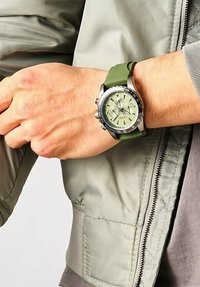 Groene siliconen strap horloge met een zilveren roestvrijstalen kast, een olijfgroene wijzerplaat en zwarte accenten; beschikt over chronograaf sub-wijzers.