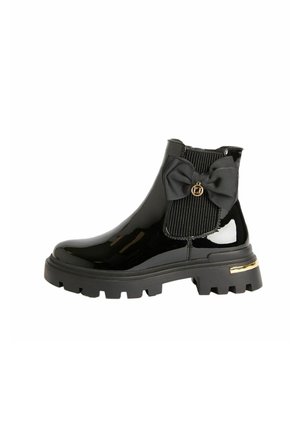 Black patent leather ankle boot with chunky sole, elastic side panel, decorative black bow, and small gold charm and heel detail.