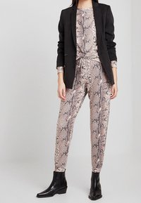 Czarna marynarka na dopasowanym, beżowym kombinezonie w wężowy wzór z przewiązanym w pasie paskiem. Całość dopełniają czarne botki do kostki.