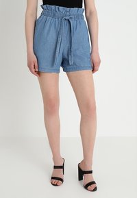 Ljusblå denimshorts med ett elastiskt, volangprytt midjeband och ett avtagbart knytbälte. Har framfickor och en avslappnad skärning.