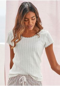 White short-sleeve top with scalloped neckline, textured pattern, and lace trim. Worn with striped pants featuring a drawstring waist.