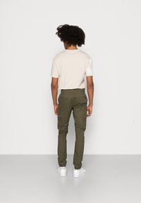 Beige t-shirt med korta ärmar, olivgröna cargobyxor med fickor och vita sneakers. Neutral bakgrund framhäver outfiten.