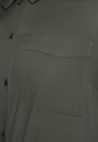 Dark green button-up shirt with a collar, featuring a chest pocket, vertical seam detailing, and a smooth, lightweight fabric texture.