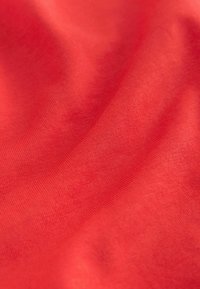 Glatka crvena tkanina s nježnim naborima i vidljivom finom teksturom tkanja.