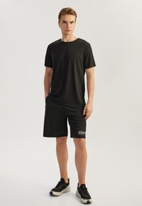 Sort atletisk t-shirt med korte ærmer og matchende shorts lavet af glat, fugttransporterende stof; outfittet har en side-logo detalje.