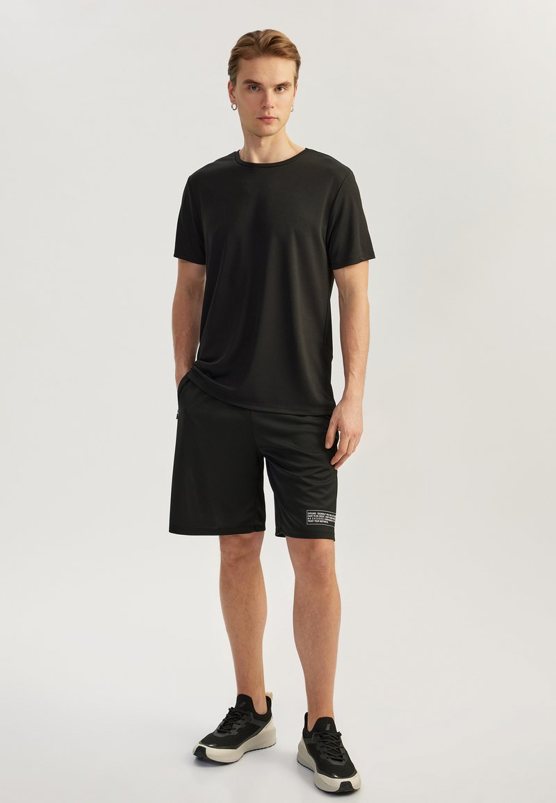 Sort atletisk t-shirt med korte ærmer og matchende shorts lavet af glat, fugttransporterende stof; outfittet har en side-logo detalje.
