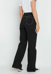 Jeans de mezclilla negra con cintura alta, corte de pierna amplia y detalles de costura blanca. Cuenta con dos bolsillos traseros y cierre de cremallera.