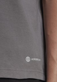 T-shirt grigio a maniche corte realizzato in tessuto morbido, con un logo "AEROREADY" bianco e un design del globo vicino all'orlo, caratterizzato da una texture liscia.