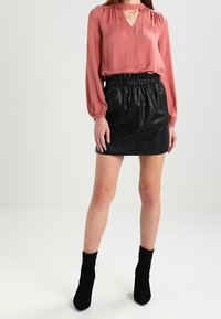 Blusa a maniche lunghe color ruggine con scollatura a V e dettagli ritagliati abbinata a una mini gonna nera in pelle sintetica con vita elasticizzata.