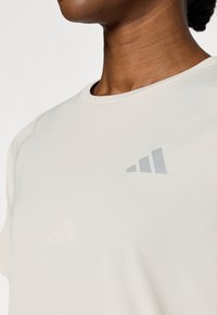 Αθλητικό t-shirt ανοιχτού μπεζ χρώ ματος, με κοντά μανίκια, κατασκευασμένο από απαλό ύφασμα, με διακριτικό γκρι λογότυπο στο πάνω αριστερό μέρος του στήθους.