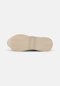 Shoe sole features a textured beige rubber with herringbone pattern, a midsole in darker tone, and branding along the center.