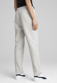 Ljusgrå sweatpants med en avslappnad passform, elastisk midja, sidofickor och slät yta, tillsammans med vita och svarta träningsskor.