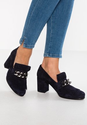 Námořnické sukové boty na blokovém podpatku s třásněmi a dekorativními kovovými akcenty. Kotníková výška s hladkým povrchem a kulatou špičkou.