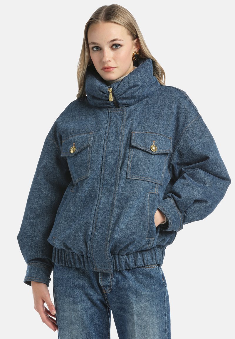 Jeans jakna z visokim ovratnikom, dvema sprednjima žepoma in rebrastim robom. Ima zadrgo in sproščen, ohlapen kroj v temno modri barvi.