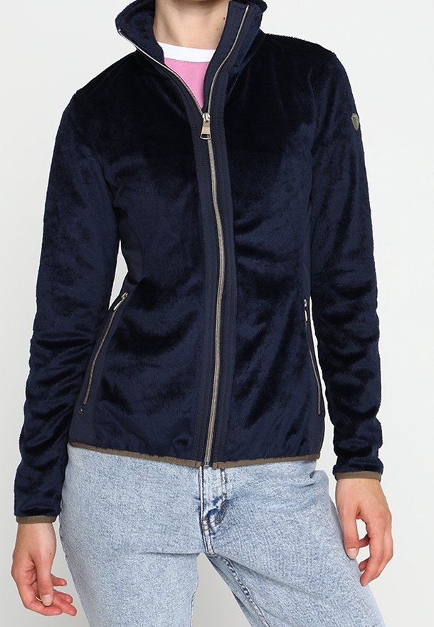 Veste polaire bleu marine à fermeture éclair avec col montant portée par une personne en jean bleu clair sur un fond uni.